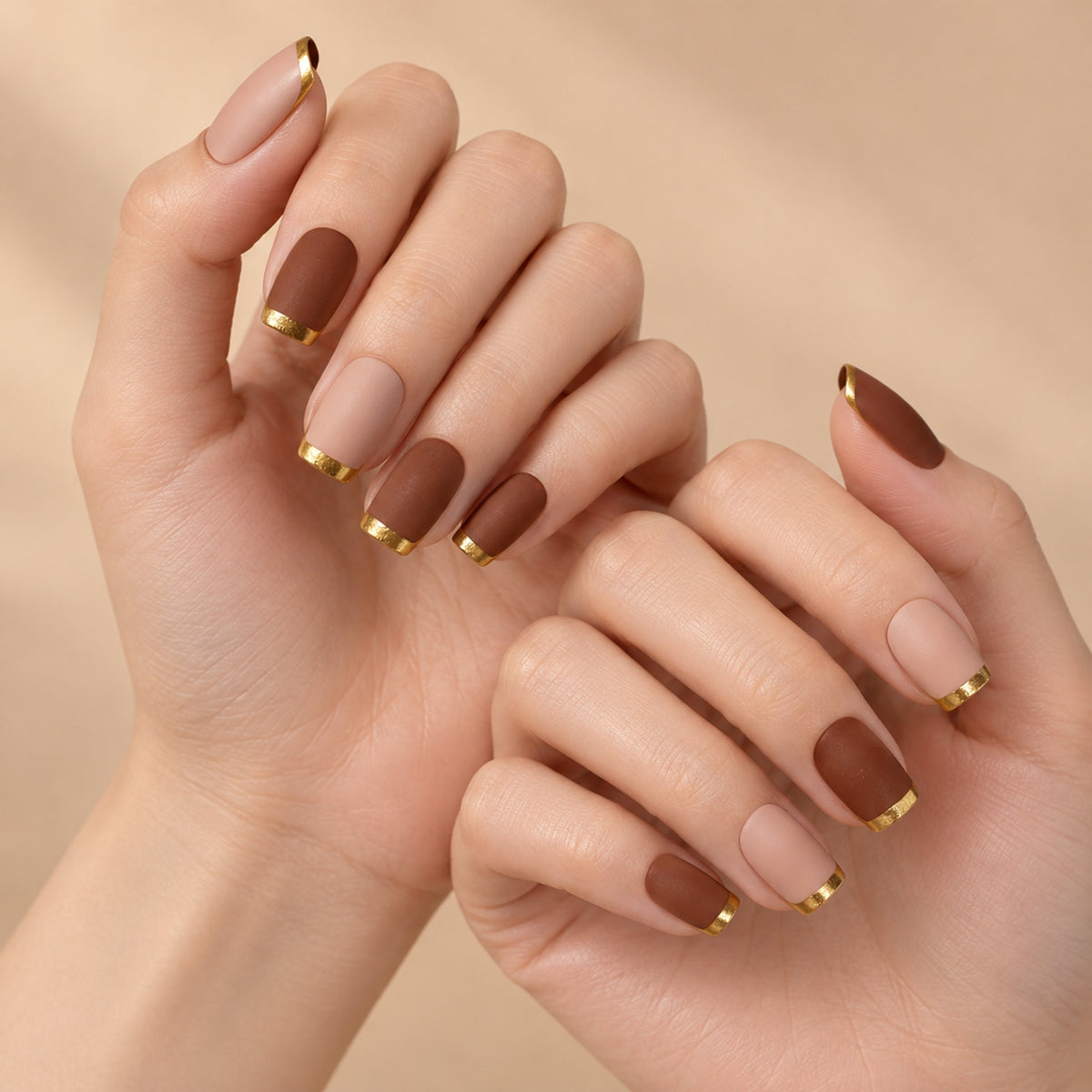 Two hands wearing matte brown and nude pink-brown nails with bright gold-coloured tips.
