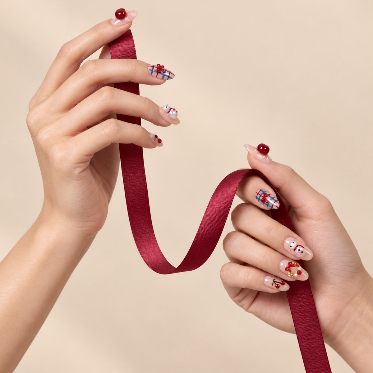 Two hands wearing cherry, plaid and snowman nail designs while holding a burgundy ribbon against a beige background.